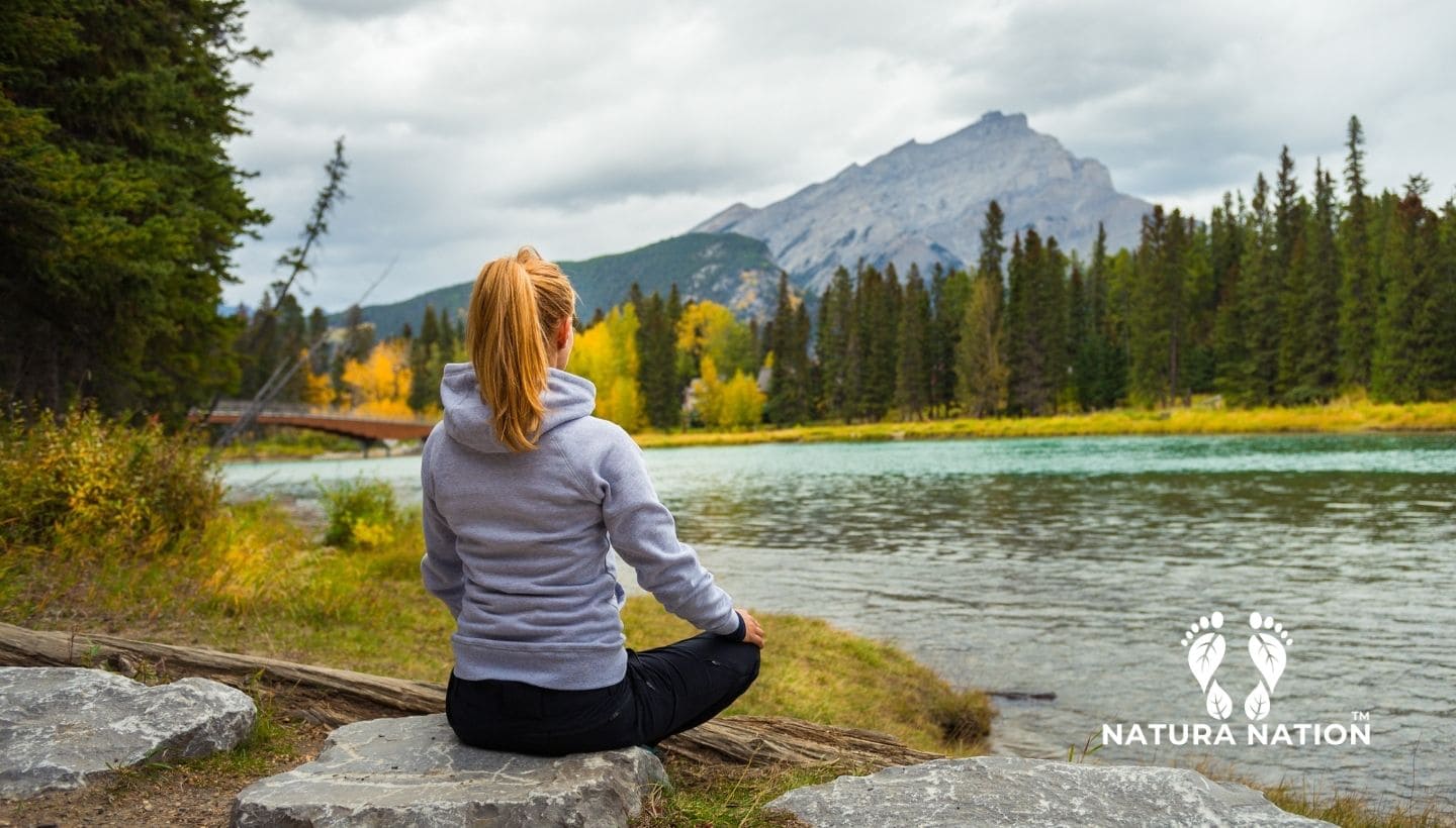 Clothing Inspired By Nature: Nature-Themed Clothing by Natura Nation. A person meditating by a lake with mountains in the background, Natura Nation logo visible.