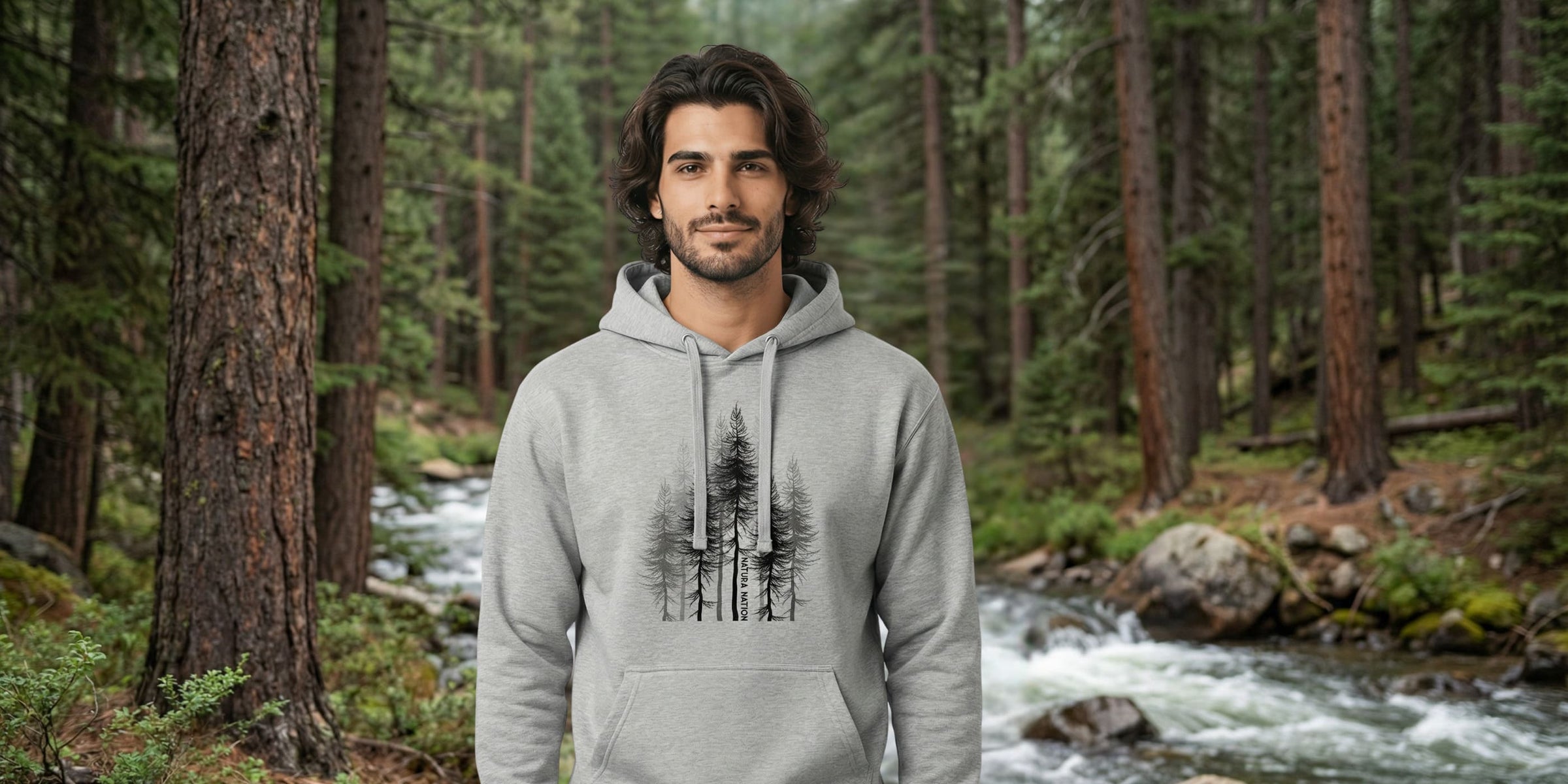 Men's Nature-Inspired Clothing — A man wearing a gray hoodie with a pine trees design by Natura Nation in a forest setting.