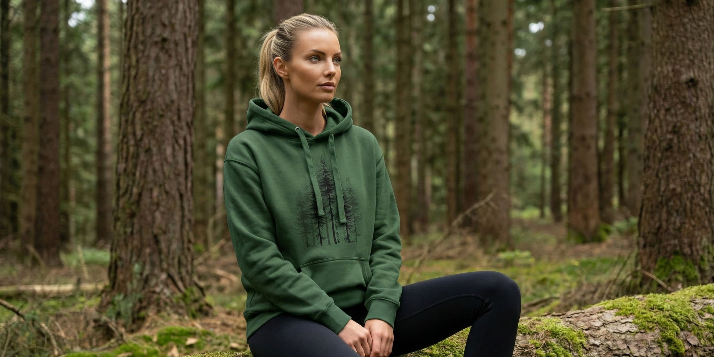 Women's Nature-Inspired Clothing - Woman in a forest green pullover hoodie designed by Natura Nation sitting on a log in a forest.