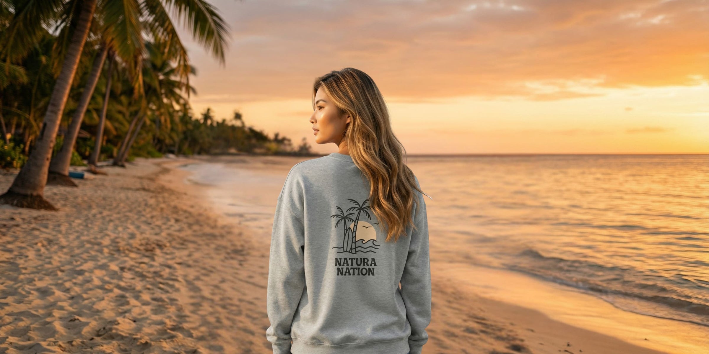 Women's Sweatshirts - A woman standing on a beach at sunset wearing a sweatshirt with a 'Natura Nation' design on the back. 